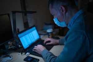 Image of man wearing surgical mask typing on a laptop computer